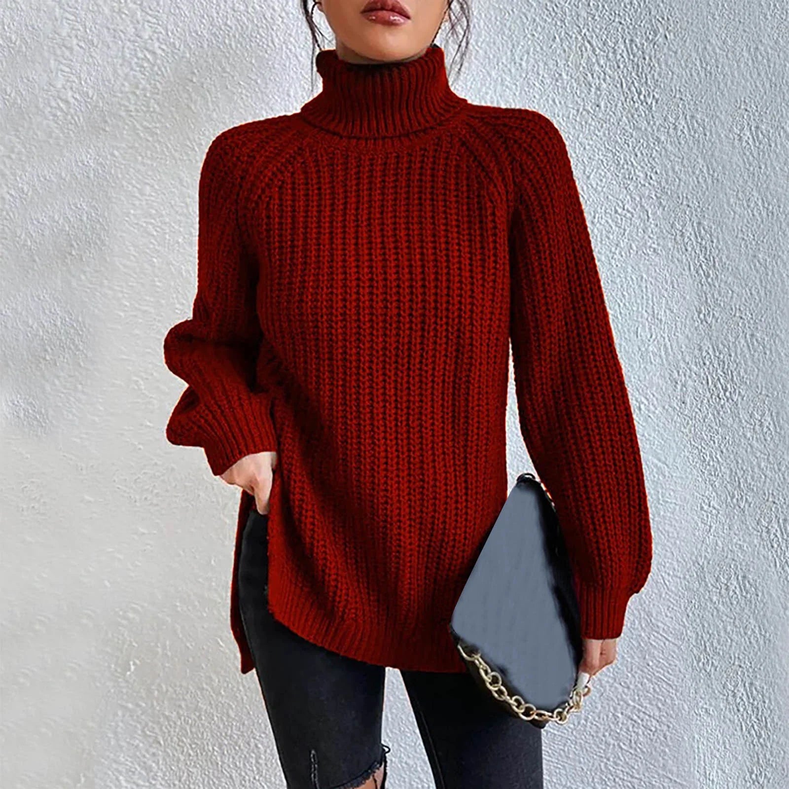 Woman wearing an oversized red turtleneck knit sweater with long sleeves, textured waffle pattern, and side slits, styled with a black quilted handbag.