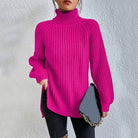 Woman wearing an oversized pink turtleneck knit sweater with long sleeves, textured waffle pattern, and side slits, styled with a black quilted handbag.