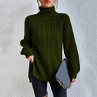Woman wearing an oversized dark green turtleneck knit sweater with long sleeves, textured waffle pattern, and side slits, styled with a black quilted handbag.