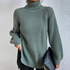 Woman wearing an oversized sage green turtleneck knit sweater with long sleeves, textured waffle pattern, and side slits, styled with a black quilted handbag.