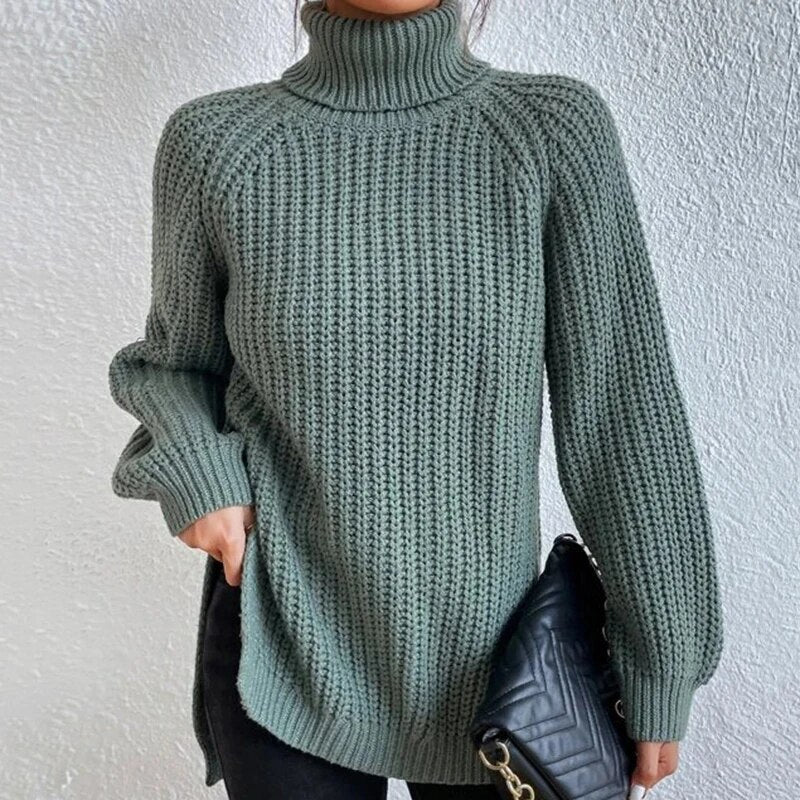 Woman wearing an oversized sage green turtleneck knit sweater with long sleeves, textured waffle pattern, and side slits, styled with a black quilted handbag.