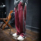 Man wearing loose maroon track pants with side stripes.