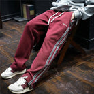 Man sitting while wearing maroon track pants with side stripes.