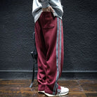 Side view of man wearing maroon track pants with grey side stripes.