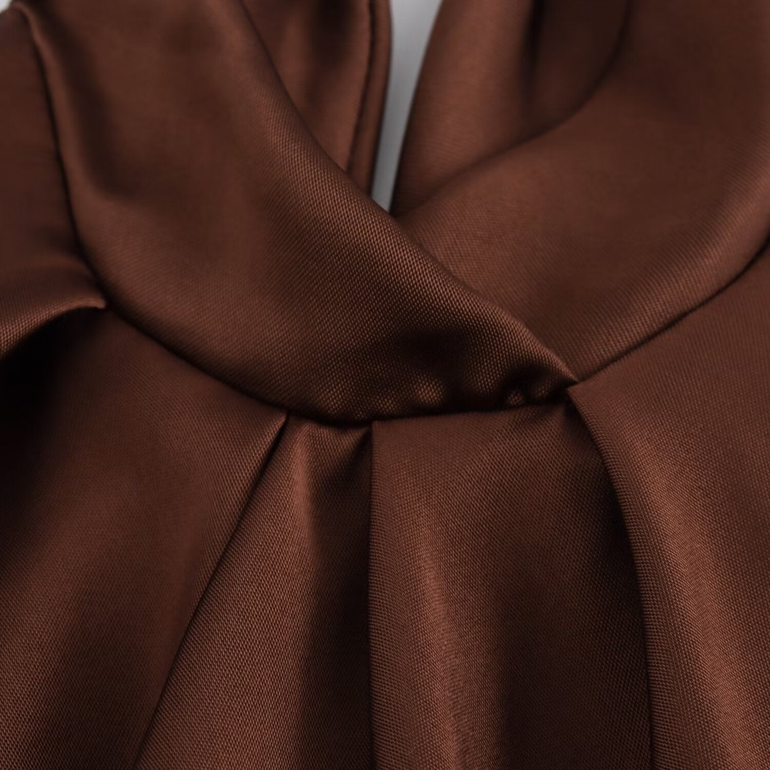 Close-up of chocolate brown fabric showing smooth, glossy texture and elegant draped folds.