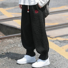 Person wearing loose black fleece jogger pants with drawstring waist and red embroidery detail, paired with white sneakers on a street.