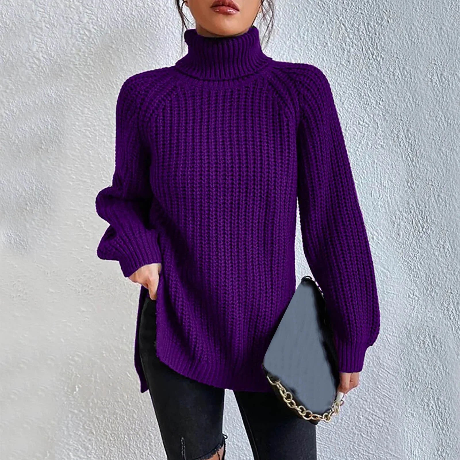 Woman wearing an oversized purple turtleneck knit sweater with long sleeves, textured waffle pattern, and side slits, styled with a black quilted handbag.