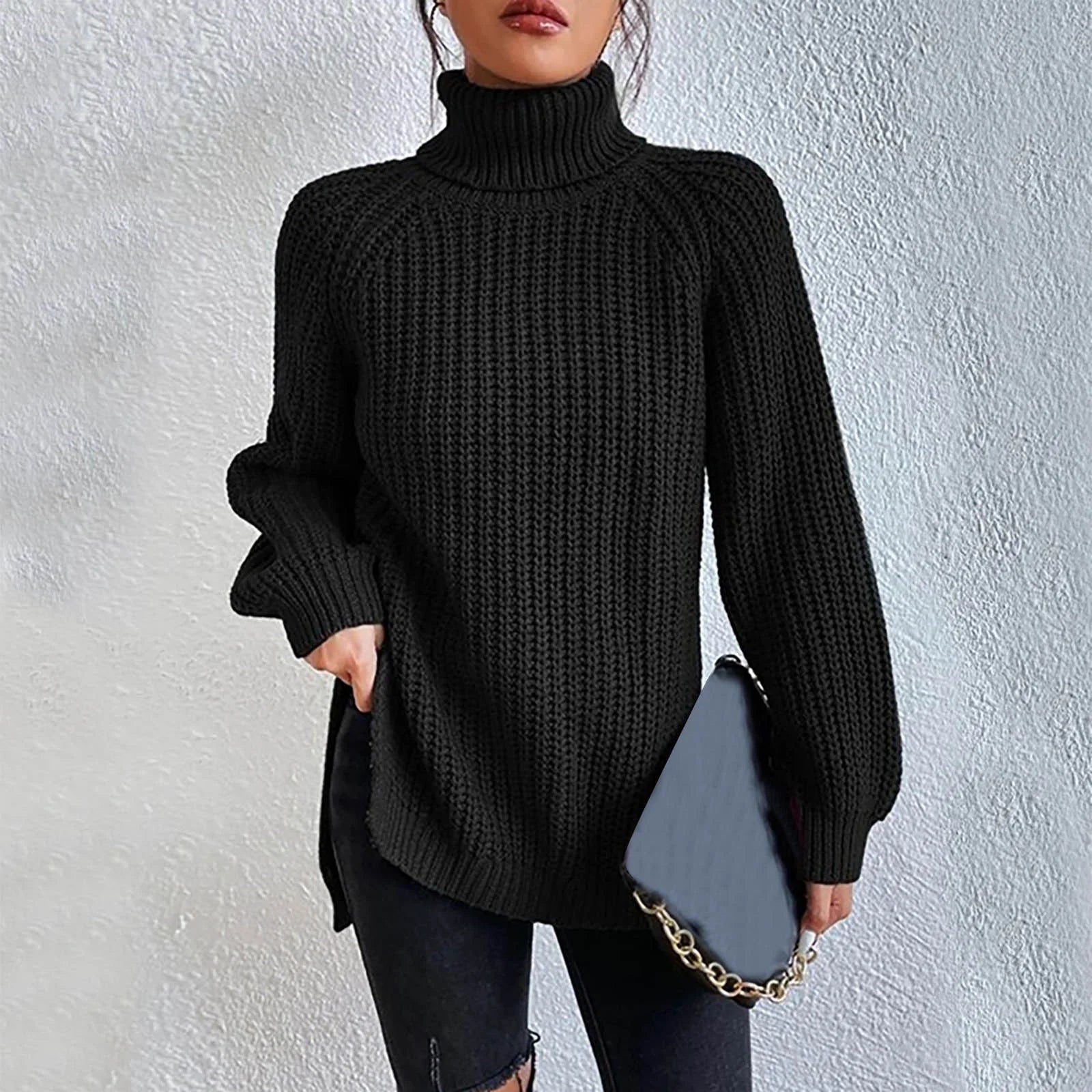 Woman wearing an oversized black turtleneck knit sweater with long sleeves, textured waffle pattern, and side slits, styled with a black quilted handbag.