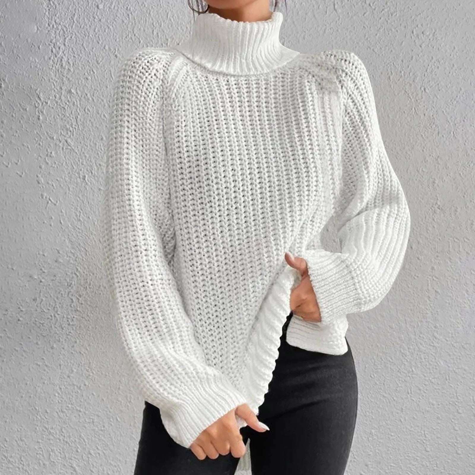 Woman wearing an oversized white turtleneck knit sweater with long sleeves, textured waffle pattern, and side slits, styled with a black quilted handbag.